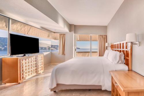 a white bedroom with a large bed and a flat screen tv at Fiesta Americana Acapulco Villas in Acapulco