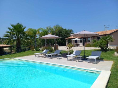 a pool with chairs and umbrellas next to a house at Villa Concita in Noto