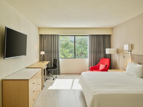 a hotel room with two beds and a desk and a red chair at Fiesta Inn Villahermosa Cencali in Villahermosa