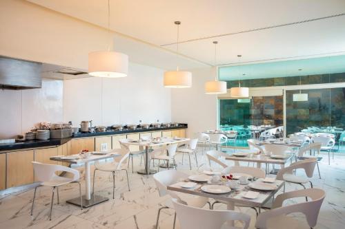 a restaurant with white tables and chairs and a kitchen at Fiesta Inn Zacatecas in Zacatecas