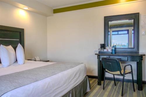 a hotel room with a bed and a desk with a mirror at Best Western Hotel Plaza Matamoros in Matamoros