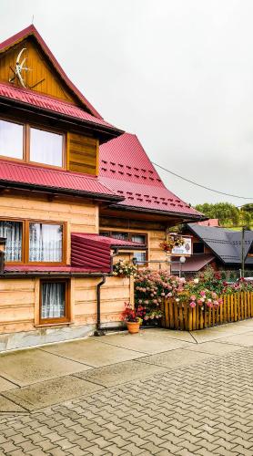 a wooden house with a red roof and some flowers at Pokoje Pod Cyrlicą u Józi in Chochołów