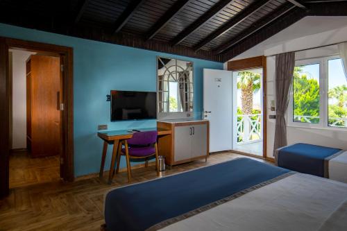 ein Schlafzimmer mit einem Bett, einem Schreibtisch und einem Fernseher in der Unterkunft Risus Beach Resort Hotel in Kusadası