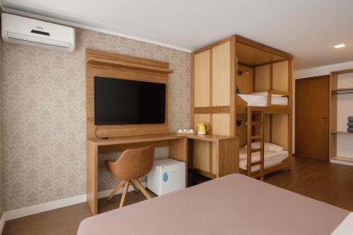 a room with a tv and a desk with a chair at Eleganz Suítes Exclusive Centro in Gramado