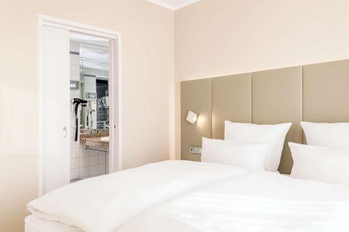 a bedroom with two white beds and a mirror at NH Dortmund in Dortmund