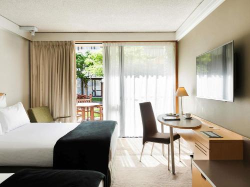 a hotel room with a bed and a desk and a table at Novotel Queenstown Lakeside in Queenstown