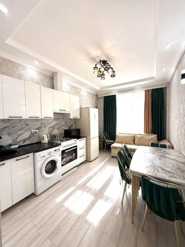 a kitchen with white cabinets and a table and a living room at жилой компекс Флоренция in Bishkek