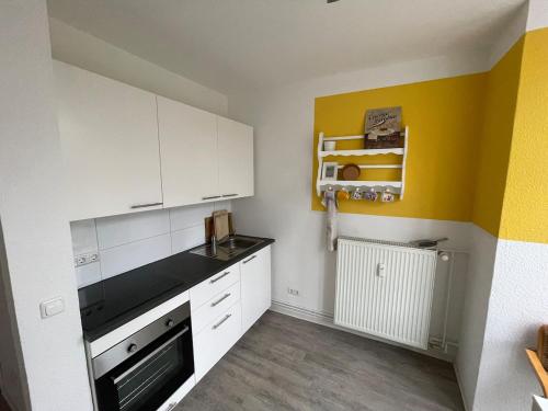 a kitchen with white cabinets and a yellow wall at Gemütliches City-Apartment in Top-Lage Hannover in Hannover