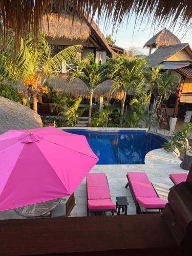 a pink umbrella and chairs next to a swimming pool at Dream Makers Retreat in Gili Air