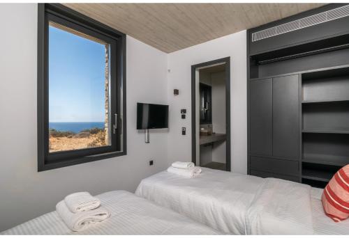 a bedroom with two beds and a window with the ocean at Hourglass Villa's Milos in Psathadika