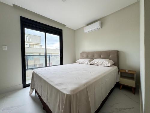 a bedroom with a large bed with a large window at Lindo apto com piscina em Bombas / SC in Bombas