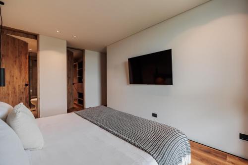 a bedroom with a white bed with a television on the wall at Kiin Living- "Child-free coliving" in Medellín