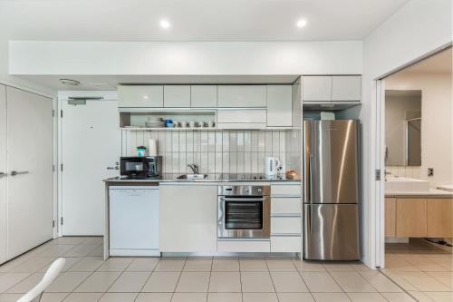 a kitchen with white cabinets and a stainless steel refrigerator at Beautiful 2BR - Pool, Gym & Parking Zodiak Stays in Auckland