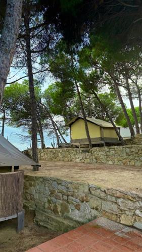 a building behind a stone wall with trees at Càmping Kanguro in San Pol de Mar