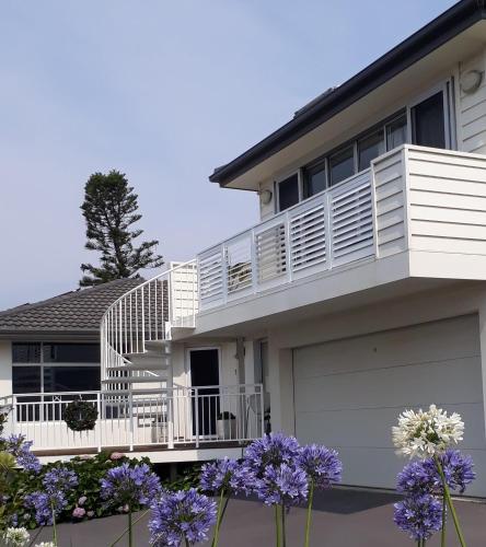 a white house with a balcony and purple flowers at Shutters Hamptons Hideaway with Sea view-Waterfront in Kiama