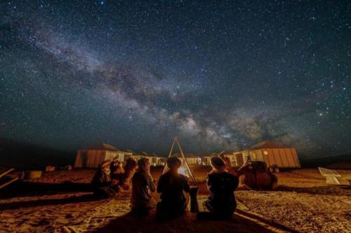 a group of people sitting on the beach looking at the stars at Merzouga Desert Tents in Merzouga