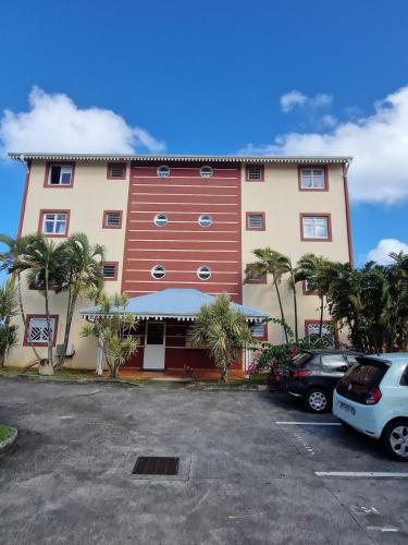 un grand bâtiment rouge avec des palmiers dans un parking dans l'établissement Superbe vue Mer, Appartement 4 personnes climatisé, Les trois ilets, Anse Mitan, à Les Trois-Îlets