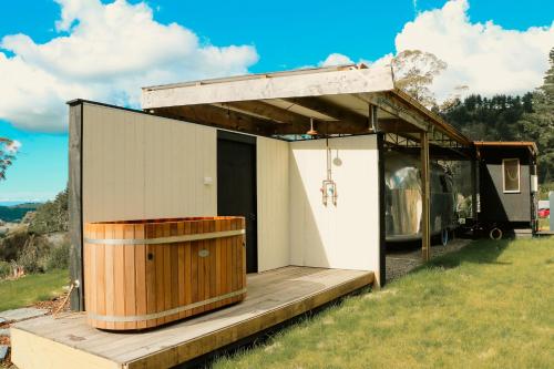 a tiny house with a wooden porch and a trailer at Airstream Caravan at Matakana Retreat in Matakana