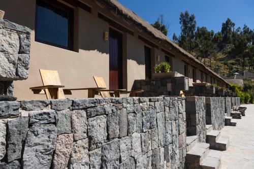 a stone wall next to a building with wooden chairs at Colca Lodge Spa & Hot Springs in Yanque