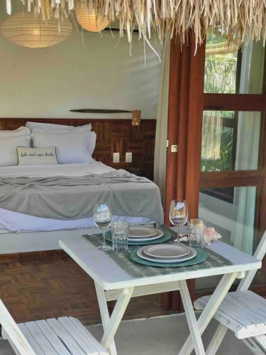 a table with plates and wine glasses and a bed at Chalé Koa Flora - PRAIA DE MOITAS in Praia de Moitas