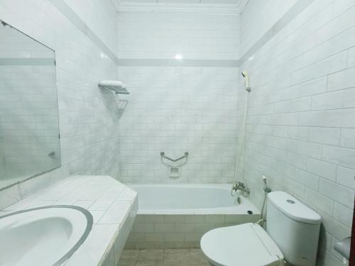 a white bathroom with a tub and a toilet and a sink at Hotel Istana Syariah Pekalongan by Hello Room in Pekalongan