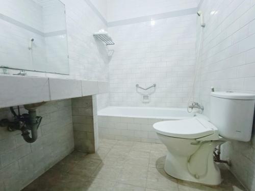 a white bathroom with a toilet and a bath tub at Hotel Istana Syariah Pekalongan by Hello Room in Pekalongan