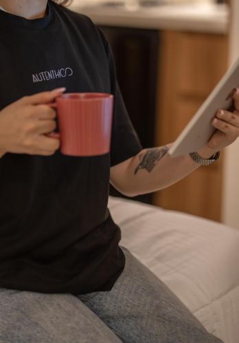 a person sitting on a bed holding a cup of coffee at Autenthico Local Stay Hotel Envigado in Envigado