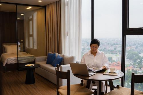 a woman sitting at a table with a laptop in a room at Mandala Hotel & Suites Hải Dương in Bảo Thap