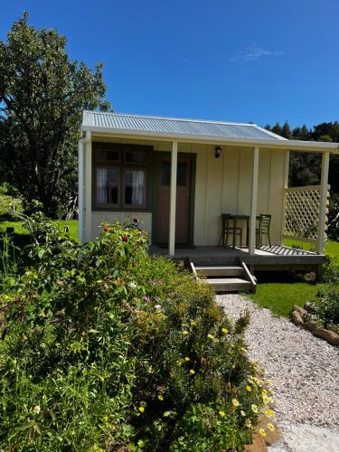 a small white house with a porch and some bushes at Wisteria Way in Opononi