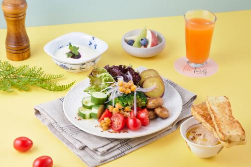 a table with a plate of food and a glass of orange juice at Two Tails Hotel Luzhou in Taipei