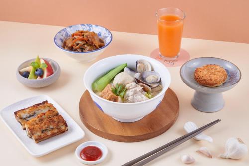 a table with bowls of food and a glass of orange juice at Two Tails Hotel Luzhou in Taipei