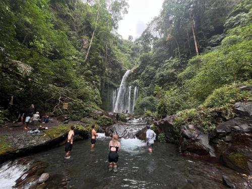 a group of people walking in the water near a waterfall at Gunung baru homestay in Senaru