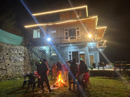 a group of people standing around a fire in front of a house at River Era by Naavagat in Jibhi