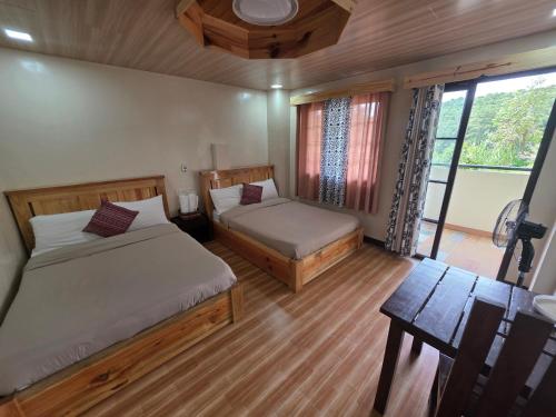 a bedroom with two beds and a table and a window at Quarrybay Hometel Sagada in Sagada