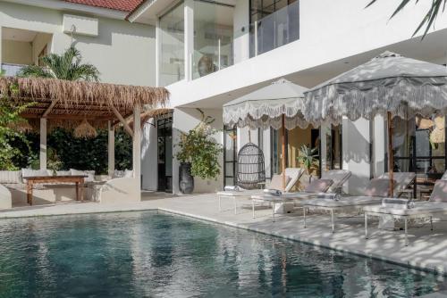 a pool with chairs and umbrellas next to a building at BI Design House Canggu in Canggu