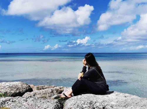 a woman sitting on a rock by the ocean at ZZOKIAI藍魚 2 mins walk to the beach! Upscale villa area 15 mins from airport! Parking, dryer, baby cots are all available in Itoman