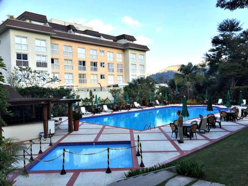 um hotel com uma grande piscina com mesas e cadeiras em Hotel Granja Brasil Resort em Itaipava