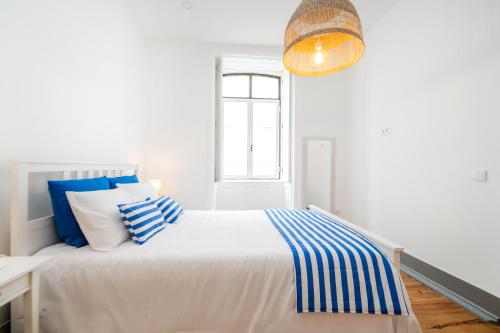 a white bedroom with a bed with blue and white pillows at Bairro Novo - Alojamento Local in Figueira da Foz