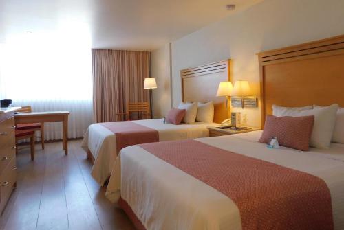 a hotel room with two beds and a desk at Hotel Palacio Azteca Tijuana, Trademark by Wyndham in Tijuana