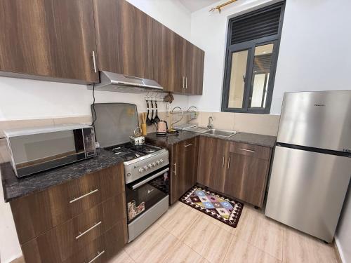 Una cocina con gabinetes de madera y un refrigerador de acero inoxidable. en Cozy 1-Bedroom Apartment at Pearl Marina, Garuga, en Entebbe