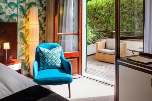 a bedroom with a blue chair and a balcony at Hotel Esplendido in Port de Soller