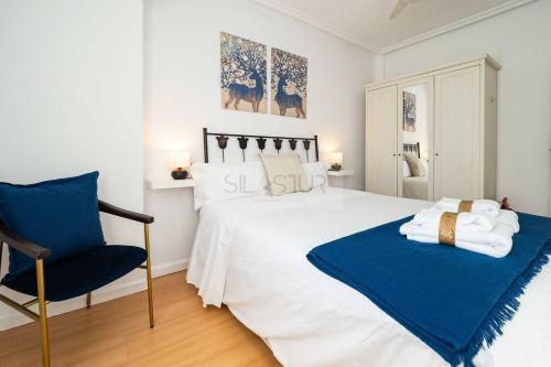 a bedroom with a white bed and a blue chair at Clave Norte By Silastur in Gijón