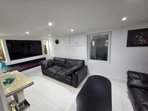 a living room with a black leather couch and a tv at Stylish 6-Bedroom House, Town Centre, Sleeps 14, With Garden in Merthyr Tydfil