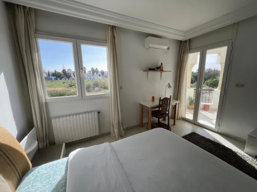 a bedroom with a bed and a desk and windows at chott meriem cozy apartment in Akouda