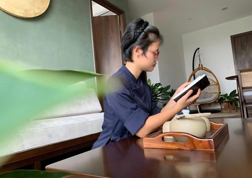 a woman sitting at a table reading a book at The inner Home, Cozy Healing Suite, Vinhomes Ocean Park in Gia Lâm Pho
