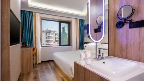 Un baño con una cama, un lavabo y un espejo. en Floral Hotel Qingdao Dreamship Seaview Hotel, en Qingdao
