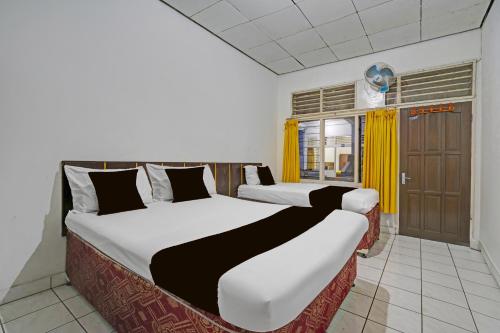 two beds in a room with yellow curtains at OYO 94802 Hotel Prima in Tjiandjur