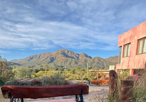 un banco frente a un edificio con montañas en el fondo en La Claudina - Cabañas Boutique en las Sierras, en Capilla del Monte