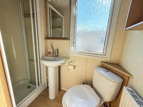 a bathroom with a toilet and a sink and a window at Cosy Caravan With Decking At Oaklands Holiday Park In Essex Ref 39042Cf in Clacton-on-Sea