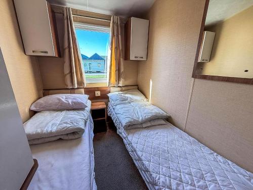 two beds in a small room with a window at Modern Caravan With Wifi At St Osyth Beach Holiday Park In Essex Ref 28010Kv in Clacton-on-Sea